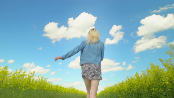 A Young Woman Runs Through a Field of Flowering Rapeseed