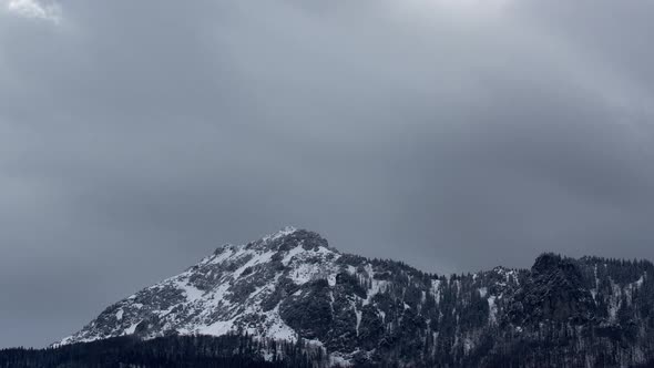 Dense clouds over a rocky snowy peak. Windy winter weather.