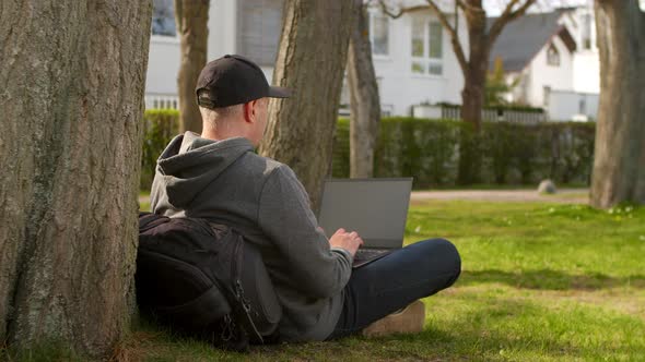 Young Man is Sitting in a Park in a Tourist Place Working on a Laptop