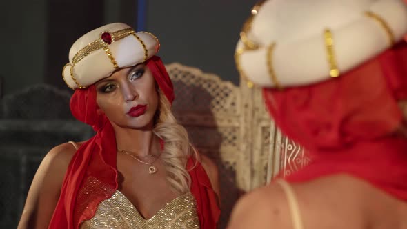 a Woman in a Turban with a Red Scarf and a Shiny Dress Carefully Examines Her Reflection in the