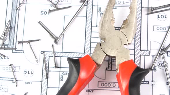 Gray and Red Pliers on Building Plan, Scheme Among Nails, Rotation, From Above
