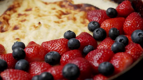 Fried Curd Pie in a Frying Pan with Strawberries and Blueberries on a Wooden Table