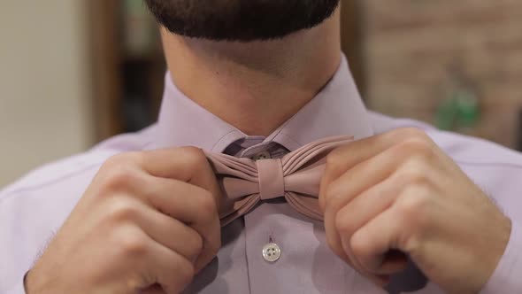 Groom Adjusts Bow Tie in Barbershop Background. Preparing To Go To the Bride