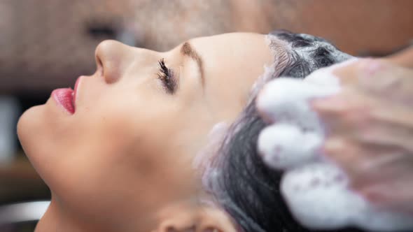 Closeup Face of Adorable Woman with Perfect Skin Enjoying Washing Hair with Shampoo By Hairdresser