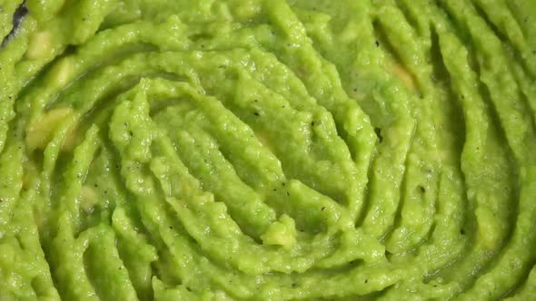 Fresh guacamole dip rotating in glass bowl close up background. Cooking healthy food