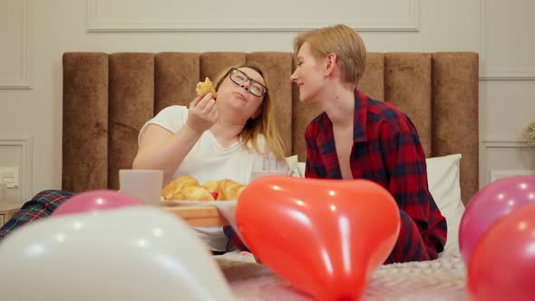 Lesbian Girls in Pajamas Lies on the Bed with Breakfast and Heartshaped Balloon