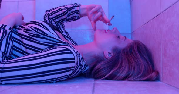 stoned young woman lying on the floor smokes a joint