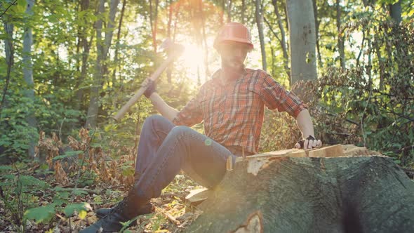 One Handsome Young Man with Beard and in Shirt Holding Wooden Axe Walking in Forest Outdoor