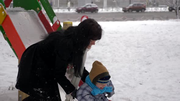 Young Beautiful Mother And Cute Child Play Outdoors During Snowfall. Winter City 11