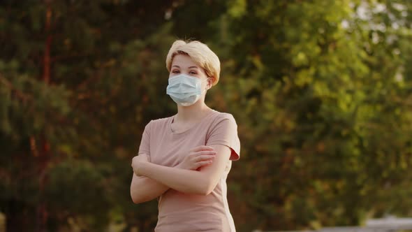 Confident Young Woman in Medical Mask Crosses Her Arms and Looks at Camera