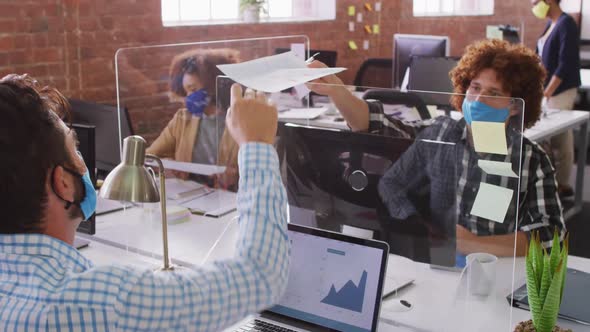 Diverse business colleagues exchanging documents over sneeze screen wearing face masks