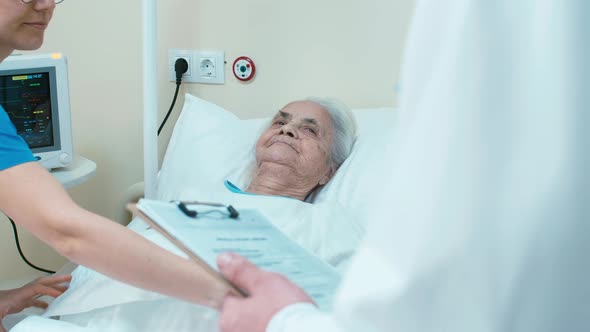 Old woman laying on hospital bed with doctor and nurse near her