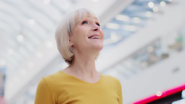 Mature Happy Caucasian Female Tourist Standing Indoor Looking Around in Amazement Attractive Elderly