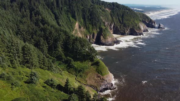 Counterclockwise drone shot of waves crashing against rocky, tree-covered cliffs on the Oregon coast
