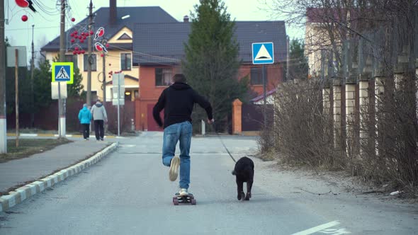 Teenager riding a skateboard and walks a dog on a leash in a sleeping area