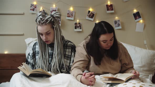 Two Girlfriends Laying in Bed and Reading Books and Holding Hands