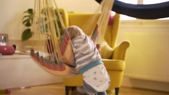 Adorable infant boy rotating in cushioned single swing at living room.
