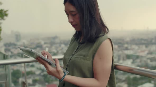 Women use tablets to chat with friends while standing beside a balcony on a rooftop.