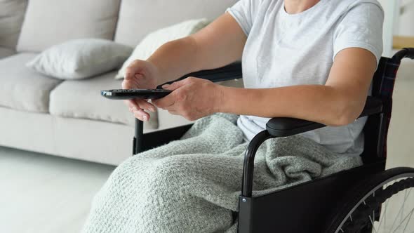 Senior Lady in Wheelchair Watching Tv in Living Room Holding Remote Control Changing Tv Channels