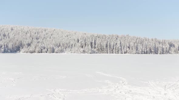 A Frozen Lake Covered with Snow with Footprint Trails  a Forest in the Background