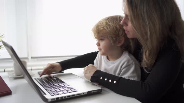 Woman with little kid working on laptop at home