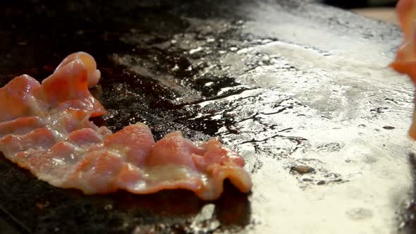 Cook Turns Bacon with Metal Tongs on the Grill