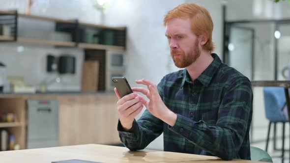 Unhappy Beard Redhead Man with Loss on Smartphone in Cafe