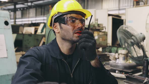 Factory Worker Talking on Portable Radio While Inspecting Machinery Parts