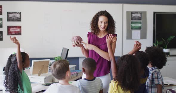 Video of happy caucasian female teacher and diverse school children studying biology in classroom