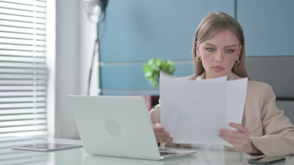 Businesswoman Reading Reports While Using Laptop