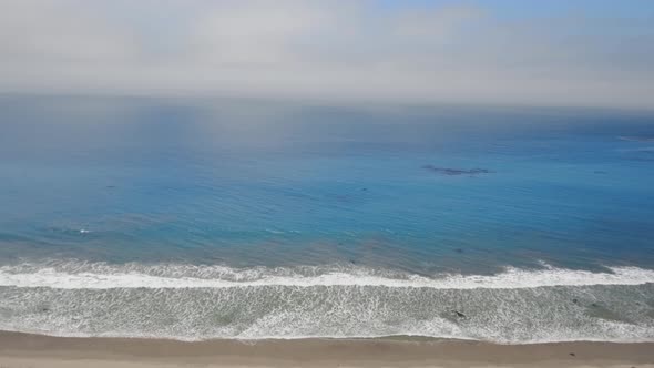 Aerial shot of foggy horizon, blue ocean and houses on the beach in Malibu, California, USA