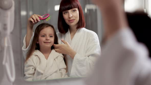 Caucasian Mother And Daughter In Bathrobes Doing Hairstyles in the Bath