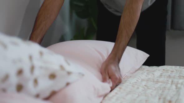 Asian man touch bedspread arranges cushions in the bedroom.
