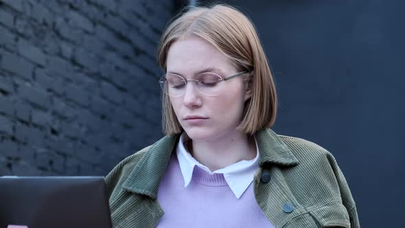 Young Woman Freelancer Sits on Cafe Terrace at Laptop