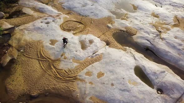 Aerial: Dirtbiker Extreme Ride Driving on Paved Stone with Sand in the River.