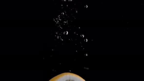 Lemon Slice Falling into Water Super Slowmotion, Black Background, lots of Air Bubbles, 4k240fps