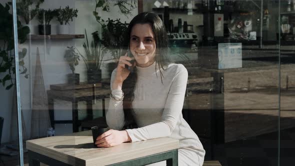 Pretty Young Woman with a Smartphone in Cafe with a Cup of Coffee Smiling