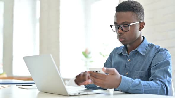 Focused Young African Man Using Laptop and Smartphone in Office