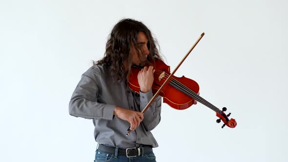Medium shot of long hair latino male musician in grey button up shirt and jeans tuning a red viola o