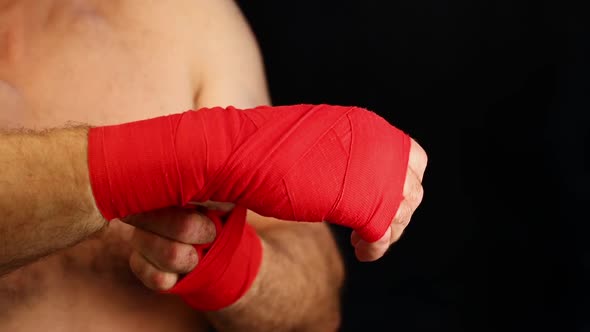 Man boxer wraps his wrists with red elastic wraps over black background