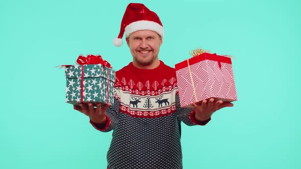 Cheerful Man in Santa Sweater Presenting Two Christmas Gift Boxes Stretches Out His Hands to Camera