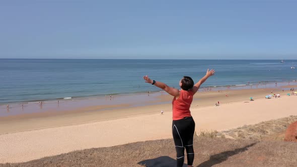 A Middleaged Woman with Her Open Arms is Doing a Warmup on the Ocean Shore