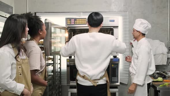 Male chef explains the electric oven to cooking class students for baking bread.