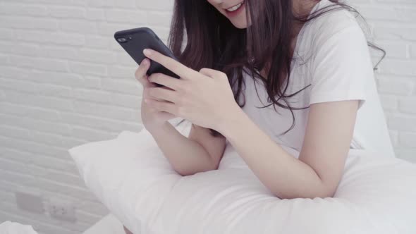 Asian woman using smartphone while lying  for texting, reading, messaging and buying online.