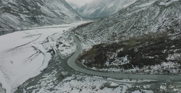 Aerial Flying Over Empty Road In Snow Covered Hunza Valley Landscape Beside Frozen River. Circle Dol