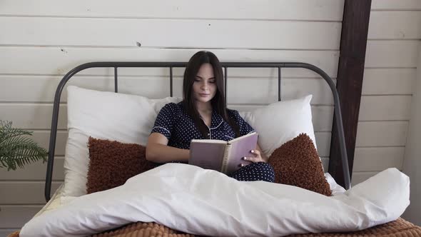 Beautiful brunette woman reading a book in bed