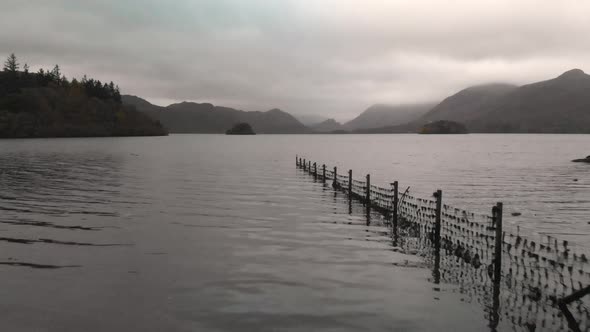 Low flying aerial shot across a fence and over a lake with mountains in the distance at sunrise.