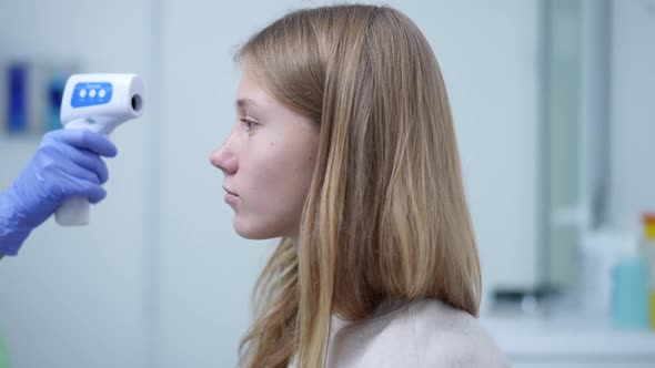 Side View Concentrated Teenage Girl Sitting in Hospital As Unrecognizable Doctor Measuring Body