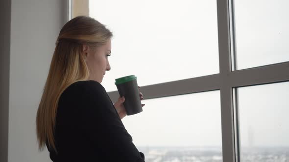 Young Woman Designer Holding in Hand Coffee Cup Drinking on Window Background