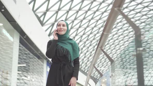 Pretty Muslim Woman in a Hijab with a Backpack Goes To the Shopping Center and Talks on the